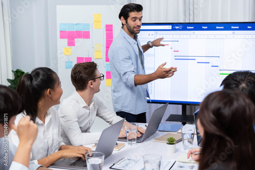 Project manager communicate and collaborate with team using project management software display on monitor, tracking progress of project task and making schedule plan at meeting table. Prudent