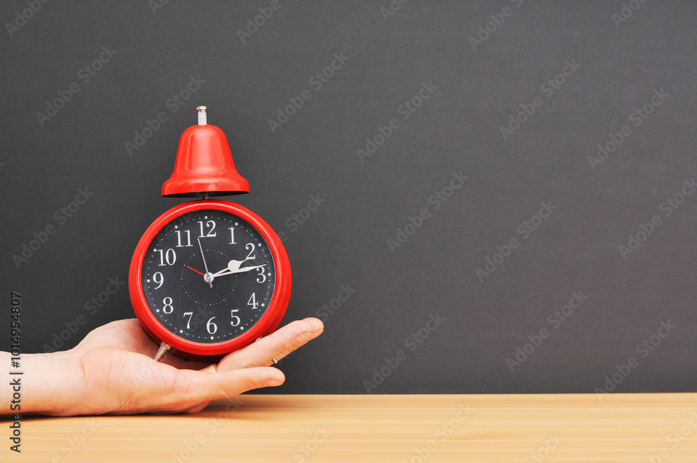 Red alarm clock on hand over wooden table with black explosion.left Red alarm clock on hand over wooden table with black explosion.left