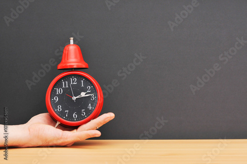 Red alarm clock on hand over wooden table with black explosion.left