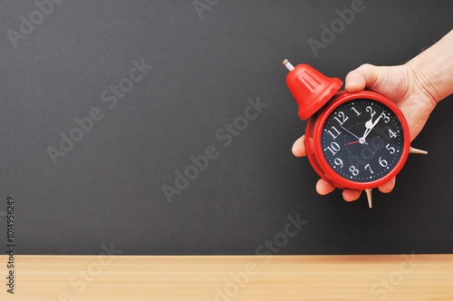 Red alarm clock in hand over wooden table with explosion background. right.