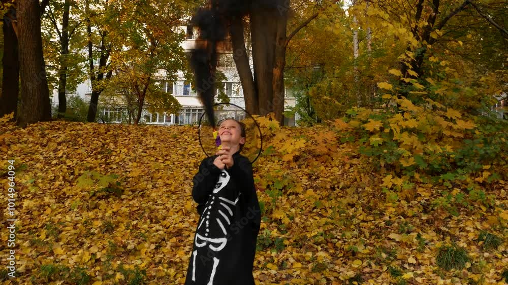 A boy in a black suit with skeleton bones painted on it and in a black hat holds a torch with black smoke in his hands against the background of an alley with yellow leaves. Celebrating Halloween. A boy in a black suit with skeleton bones painted on it and in a black hat holds a torch with black smoke in his hands against the background of an alley with yellow leaves. Celebrating Halloween.