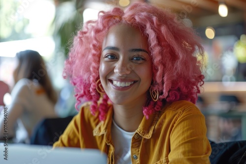 A woman with bright pink hair sits comfortably in front of a laptop, focused on her work