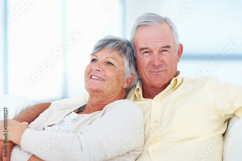 Old couple, portrait and hug in home, security and love in marriage connection on couch. Elderly people, embrace and commitment to relationship in retirement, bonding and support for comfort on sofa