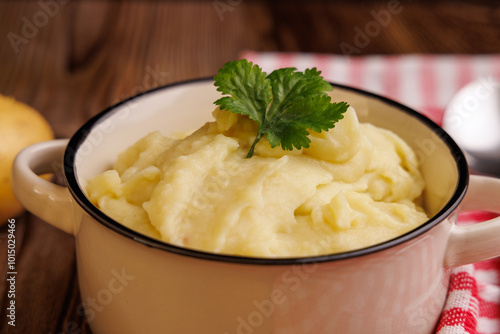 Top View of Mashed Potatoes in a Bowl with Potatoes, Spoon, and Red Napkin on Wooden Table