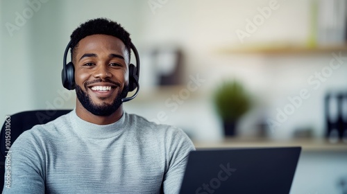 Smiling person with headphones working on a laptop in a bright office environment.