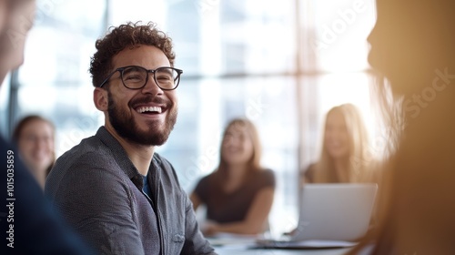 Happy man with glasses smiling in a group meeting with bright, modern interior.