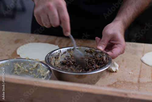 Horizontal photo. Man spoons meat onto dough. Male hand close up. Chef prepares khinkali, dumplings, ravioli on wooden table at counter of cafe. City Day. Street fair. Food festival. Tbilisoba holiday