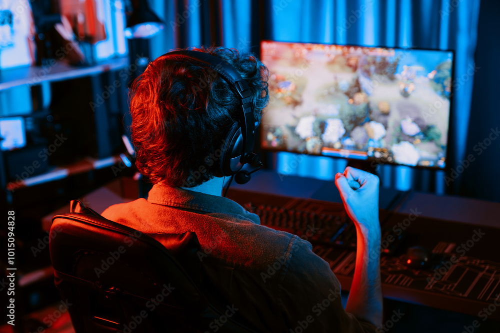 Obraz premium Host channel of young gaming streamer getting to win fighting Moba at battle arena with multiplays team, wearing headphone on pc monitor with back side image at neon digital light modern room. Gusher.