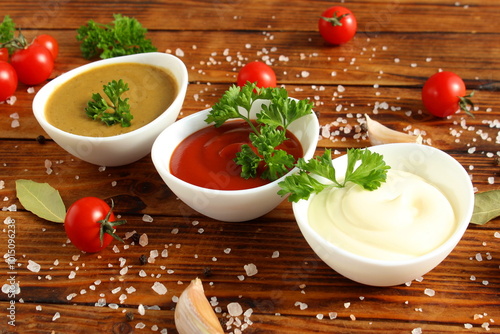 There are three bowls of mayonnaise, ketchup and mustard on a wooden table. photo