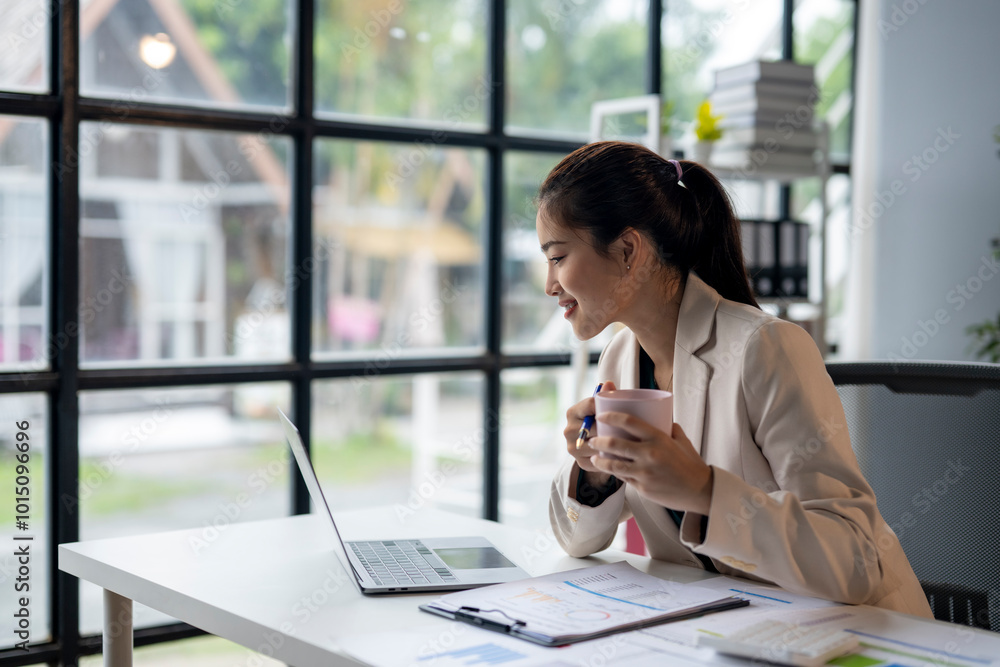 A woman is sitting at a desk with a laptop and a cup of coffee A woman is sitting at a desk with a laptop and a cup of coffee