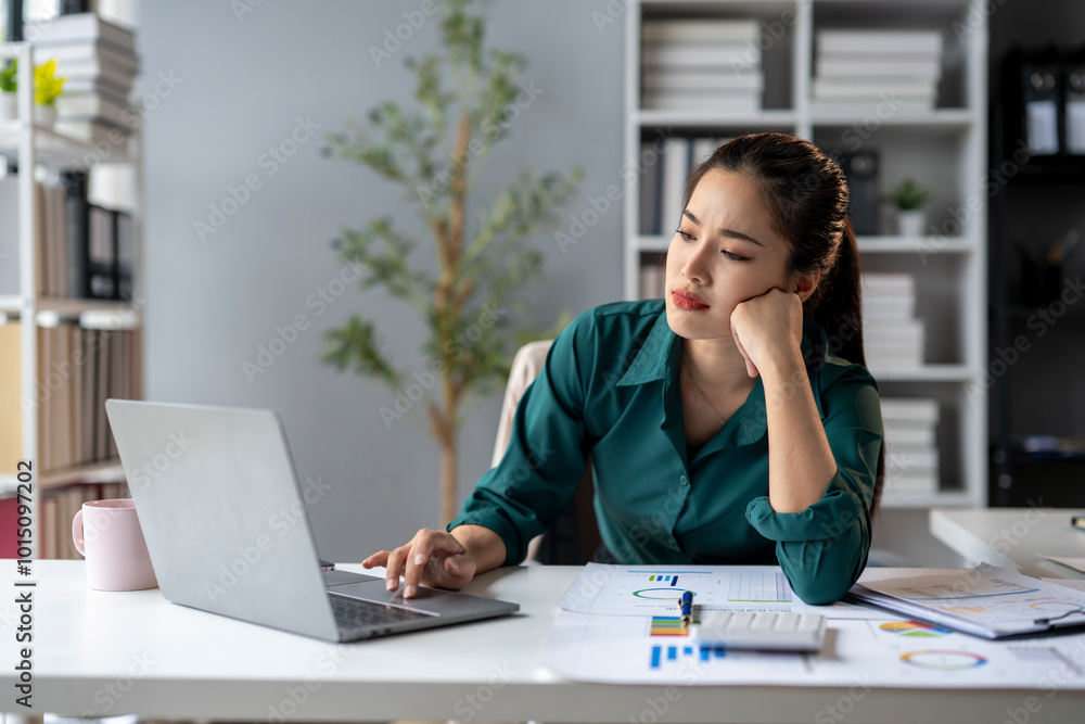A woman is sitting at a desk with a laptop and a stack of papers A woman is sitting at a desk with a laptop and a stack of papers
