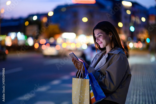 Bild auf Leinwand Elegant woman browsing on smartphone after shopping spree in city at night