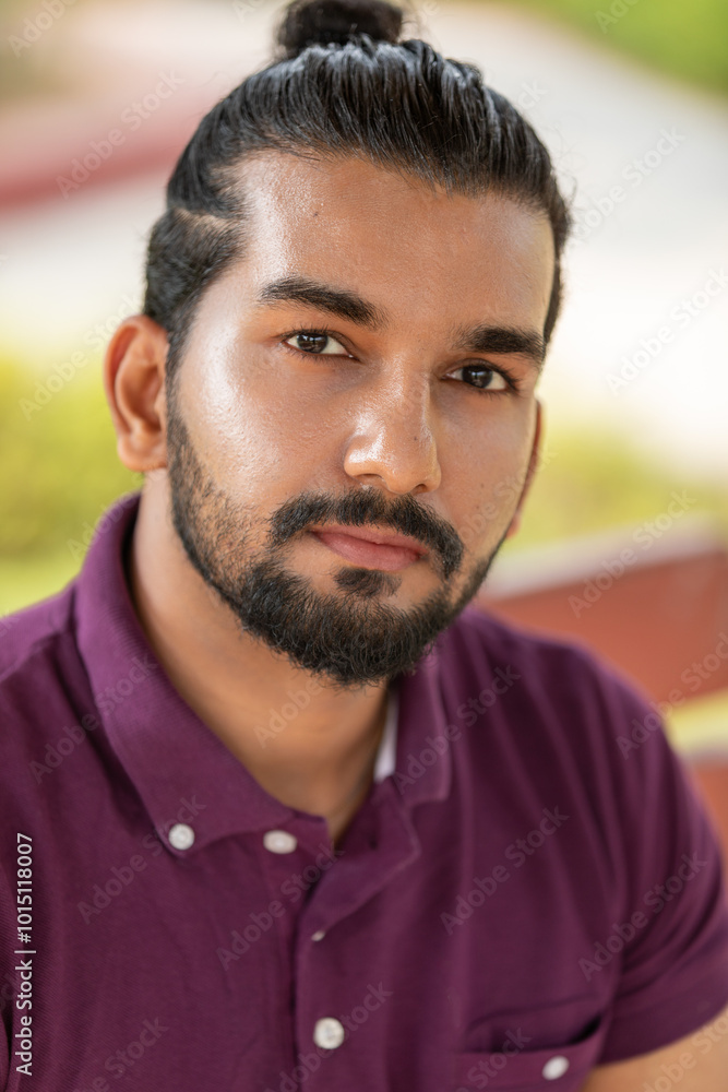 Fototapeta premium Close-up portrait of a confident, handsome, bearded Asian-Indian man with a ponytail. He faces the camera, showing a range of facial expressions and exuding a calm demeanor.