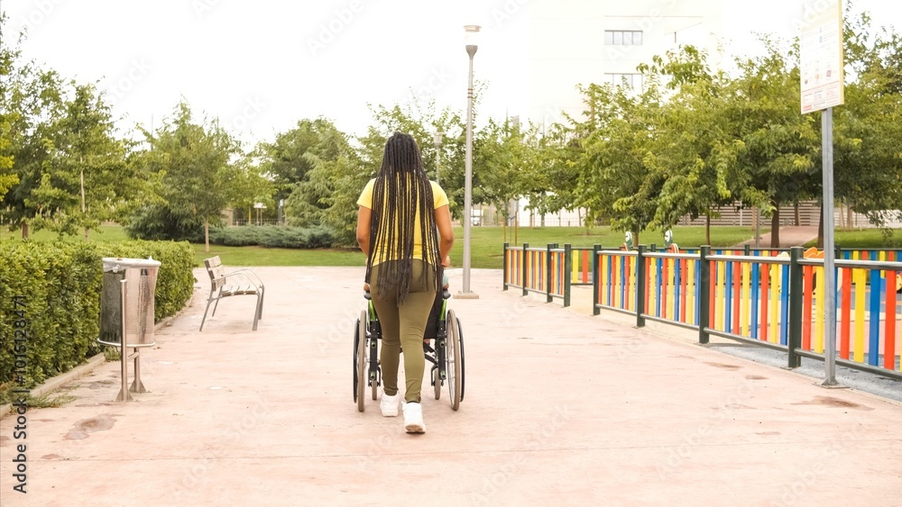 Back view of woman pushing handicapped brother in wheelchair on footpath at park Back view of woman pushing handicapped brother in wheelchair on footpath at park