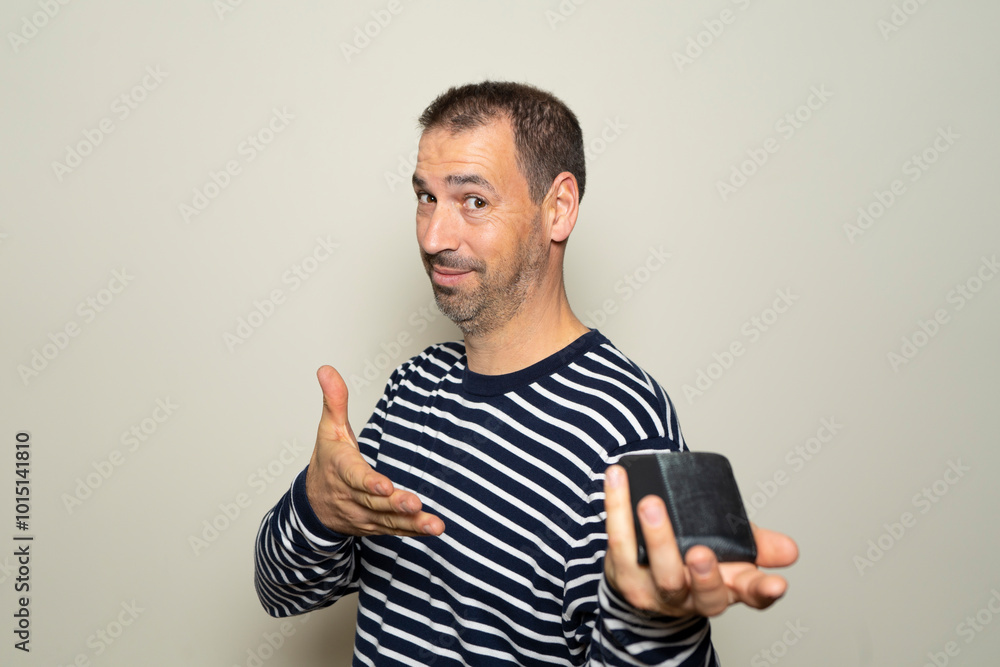 Bearded hispanic man in his 40s wearing a ryas sweater happily and proudly offering his wallet full of money, isolated over beige background. Bearded hispanic man in his 40s wearing a ryas sweater happily and proudly offering his wallet full of money, isolated over beige background.