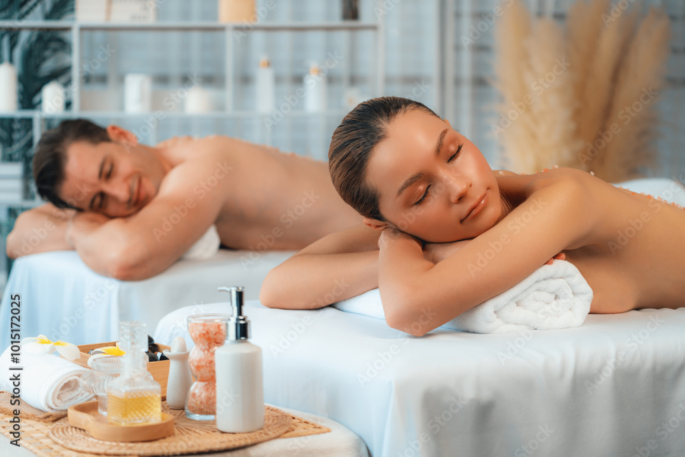 Blissful couple customer having exfoliation treatment in luxury spa salon with warmth candle light ambient. Salt scrub beauty treatment in health spa body scrub. Quiescent Blissful couple customer having exfoliation treatment in luxury spa salon with warmth candle light ambient. Salt scrub beauty treatment in health spa body scrub. Quiescent