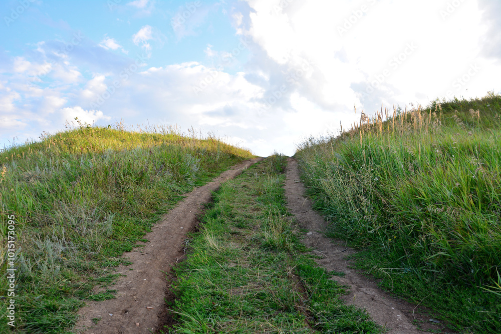 a dirt country road leads to a grassy hill with the light in the background a dirt country road leads to a grassy hill with the light in the background