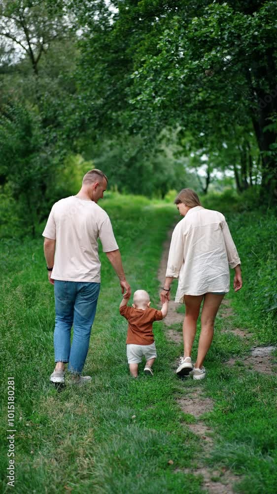 Rear view of a Caucasian couple with their little baby on the walk. Loving mom and dad leading their son by the green grass. Vertical video. Rear view of a Caucasian couple with their little baby on the walk. Loving mom and dad leading their son by the green grass. Vertical video.