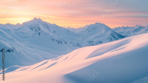 A majestic mountain range is bathed in the soft glow of a pink sunrise. The snow-covered peaks are a breathtaking sight against the clear, blue sky.