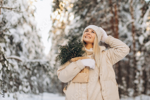 Happy young woman in warm cozy clothes with pine branches in craft paper against the background of snowy winter forest.