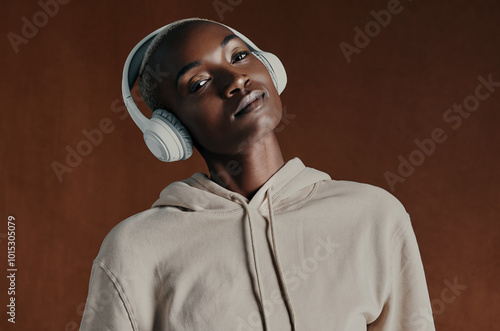 Black woman, hoodie and headphones for music in studio portrait, training and fitness by background. Person, model and style with jacket, streetwear and streaming with clothes for winter in Nigeria photo