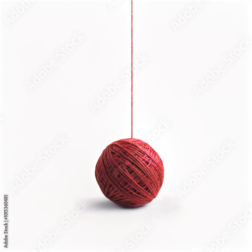 A vibrant red ball of yarn with an unspooled thread resting on a white surface