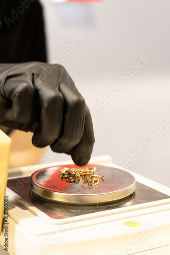 Selective focus of weighing gold jewelry with small digital scales in jewelry shop. Hand take jewelry on the digital scale, close up. Hand in black glove puts gold on scales.