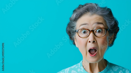 Shocked Elderly Asian Woman in Glasses with Teal Background photo