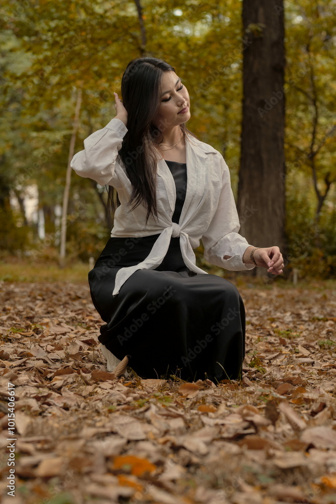 A beautiful young girl in a white blouse and a long black skirt is posing in an autumn park. A beautiful young girl in a white blouse and a long black skirt is posing in an autumn park.