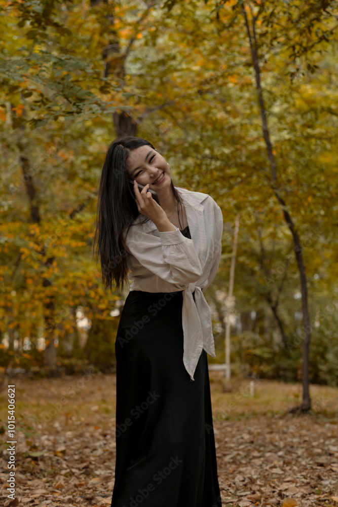 A beautiful young girl in a white blouse is talking on the phone in an autumn park. A beautiful young girl in a white blouse is talking on the phone in an autumn park.