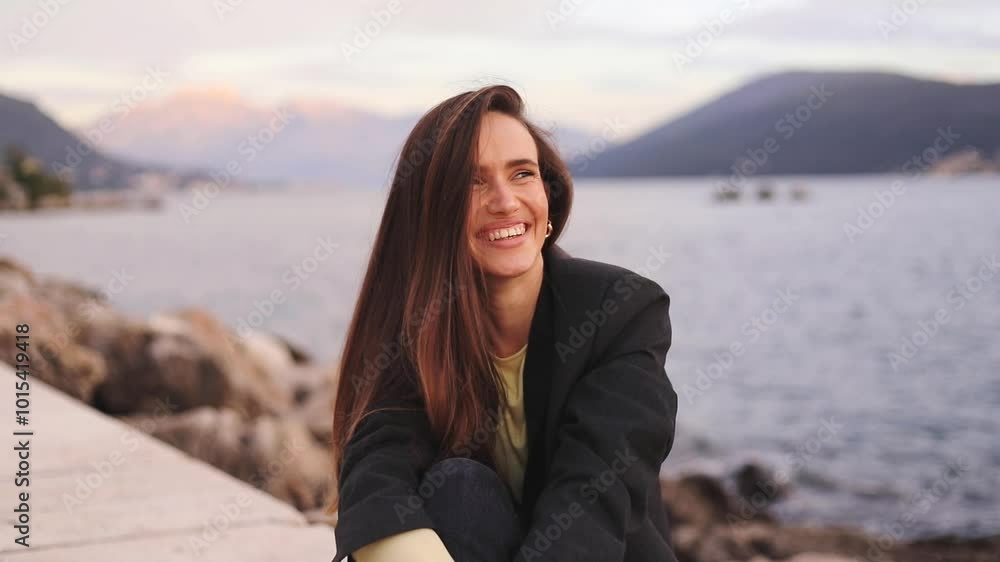 Portrait, woman smiling sitting near sea, vacation and travel on holiday in sunset outdoors. Happy face, laughing girl relax at sea, ocean and freedom, wellness and nature. Woman wear jacket. Portrait, woman smiling sitting near sea, vacation and travel on holiday in sunset outdoors. Happy face, laughing girl relax at sea, ocean and freedom, wellness and nature. Woman wear jacket.