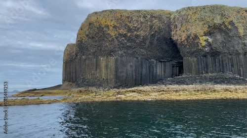 Impressive basalt formation with a cave on the coast, surrounded by deep blue sea and cloudy sky, Fingal's Cave, Staffa, Inner Hebrides, Scotland, United Kingdom, Europe