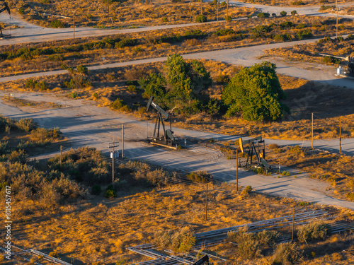 Aerial perspective of an oil field in California's desert, featuring pumpjacks and dirt roads amidst sparse vegetation and arid terrain.
