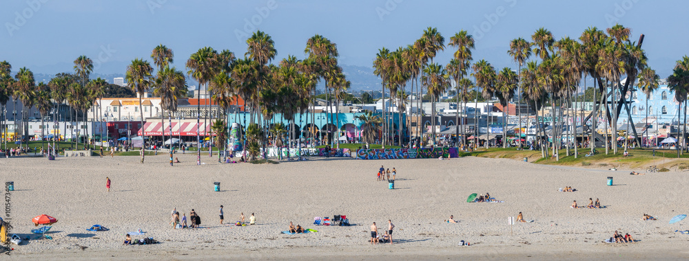 Venice Beach in Los Angeles features a wide sandy shore, iconic palm trees, and colorful buildings. People are sunbathing under the sunny sky. Venice Beach in Los Angeles features a wide sandy shore, iconic palm trees, and colorful buildings. People are sunbathing under the sunny sky.