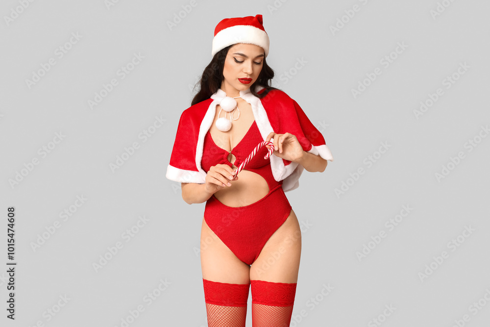 Obraz premium Beautiful young sexy woman in lingerie and Santa hat with candy cane on grey background