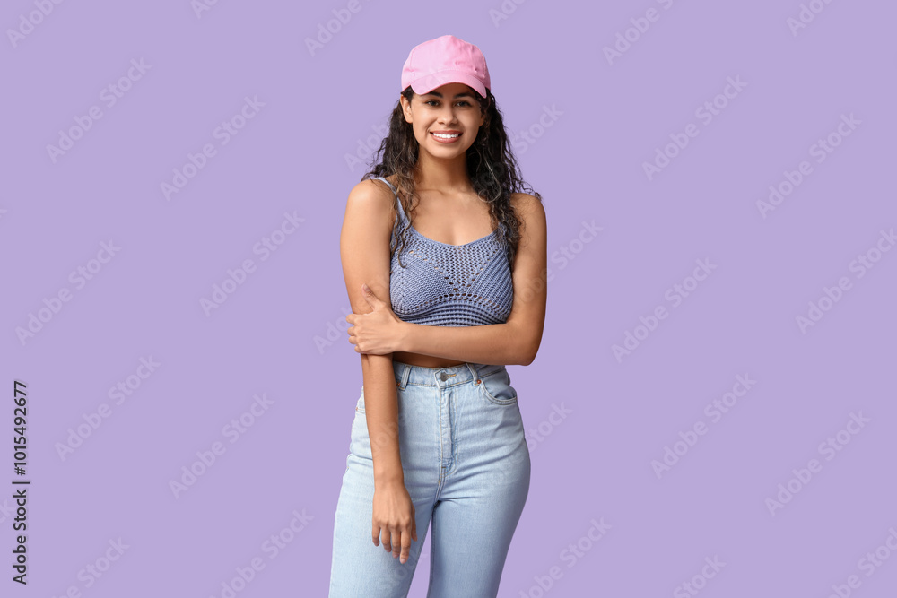 Stylish African-American woman wearing top, jeans and cap on lilac background Stylish African-American woman wearing top, jeans and cap on lilac background