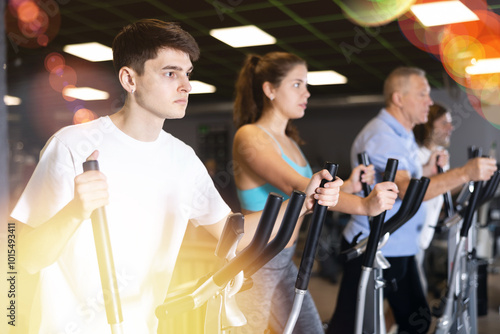 Group of athletic people of different ages train on elliptical trainers steppers