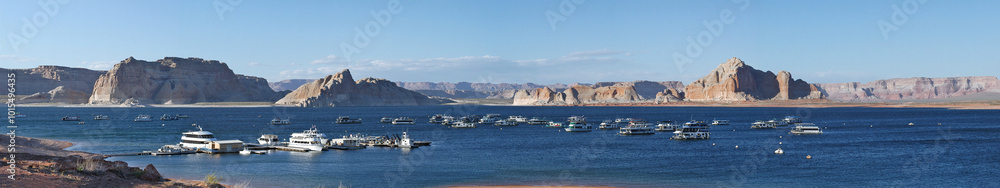 Panoramic view of Lake Powell with numerous boats floating on the calm blue water, surrounded by majestic sandstone formations. A popular recreation spot with stunning desert and lake scenery. Panoramic view of Lake Powell with numerous boats floating on the calm blue water, surrounded by majestic sandstone formations. A popular recreation spot with stunning desert and lake scenery.