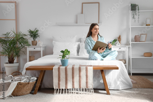 Young woman in pajamas reading magazine on bed at home photo