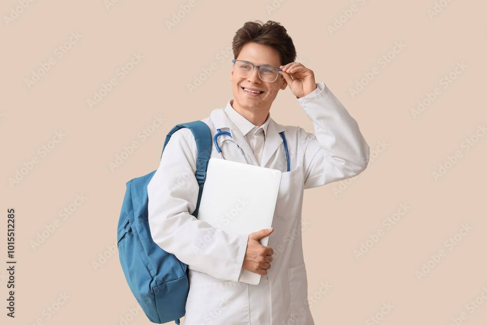 Male medical intern with backpack and laptop on beige background Male medical intern with backpack and laptop on beige background