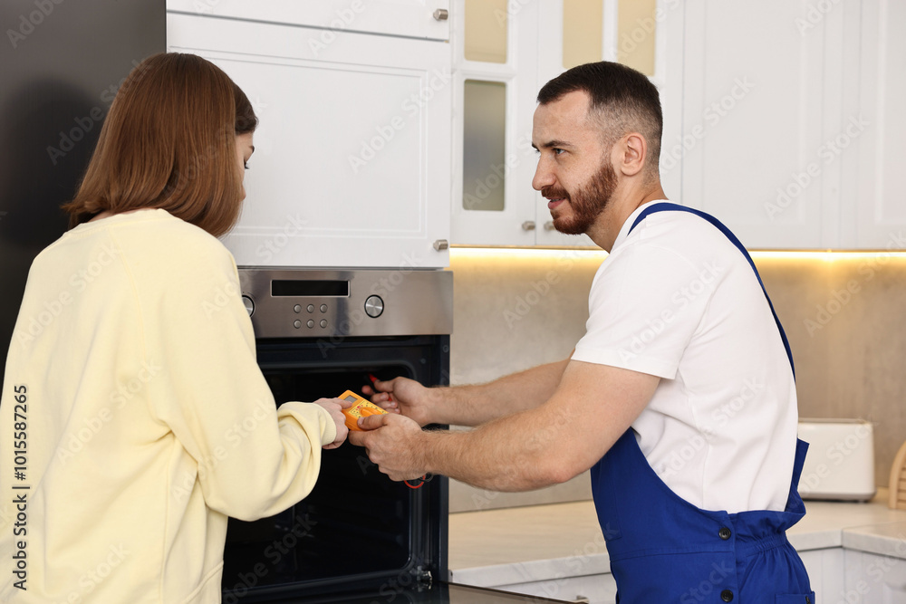 Repairman showing woman how to use multimeter near oven in kitchen Repairman showing woman how to use multimeter near oven in kitchen