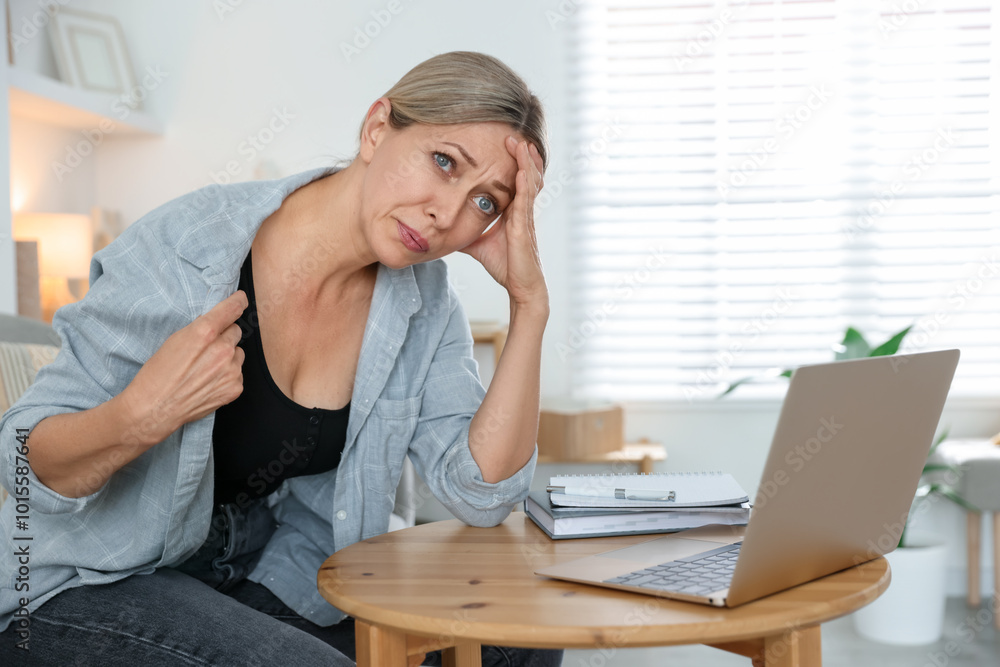 Menopause. Woman suffering from hot flash at table with laptop indoors Menopause. Woman suffering from hot flash at table with laptop indoors