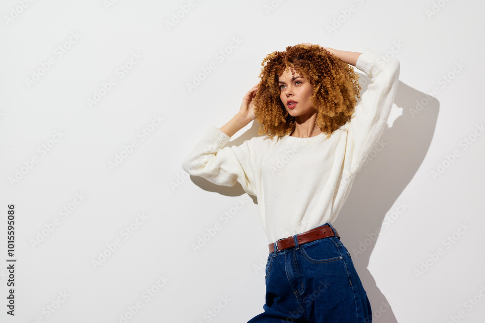© SHOTPRIME STUDIO - Fashion portrait of a young woman with curly hair wearing a stylish white sweater and high waisted jeans against a minimalist white background © SHOTPRIME STUDIO - Fashion portrait of a young woman with curly hair wearing a stylish white sweater and high waisted jeans against a minimalist white background