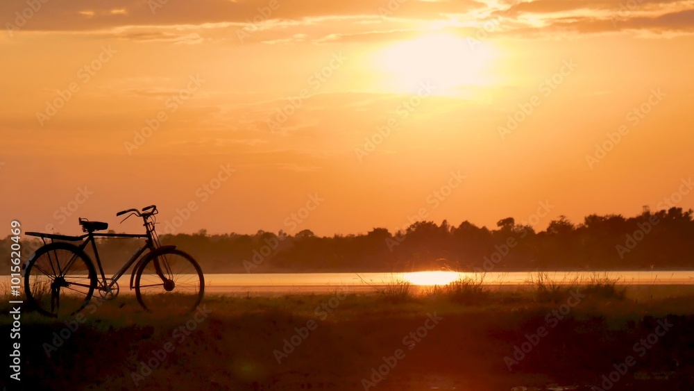 Fototapeta premium Silhouette bicycle sunset golden sky background. Bike park in nature garden outdoors country leisure lake view on sunrise water reflection sunbeam at dawn. Silhouette bicycle biking golden landscape