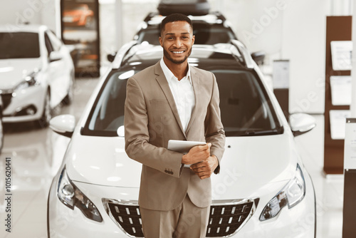 Cars Dealership Concept. Auto Seller Afro Man Smiling To Camera Standing In Automobile Center.