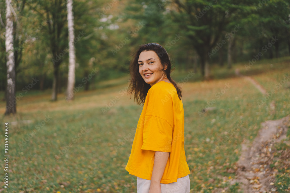 A woman in a bright yellow top walks through a park, smiling happily as she enjoys the beauty of nature and the warmth of the sun in autumn. A woman in a bright yellow top walks through a park, smiling happily as she enjoys the beauty of nature and the warmth of the sun in autumn.