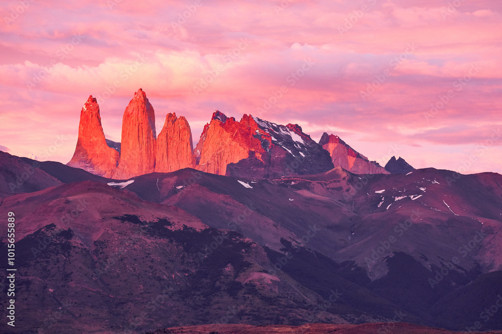 Naklejka premium Torres del Paine in Patagonia, Chile, bathed in the warm glow of a sunrise, with the iconic granite spires illuminated in shades of pink and red against the morning sky.