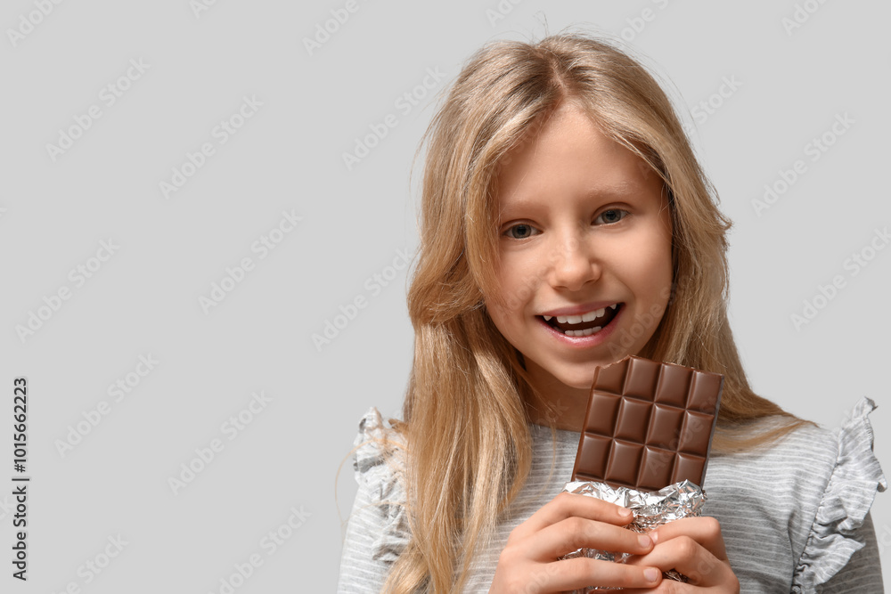 Cute little girl with sweet chocolate bar on grey background Cute little girl with sweet chocolate bar on grey background