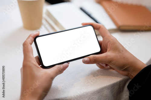 Close-up of a woman holding a smartphone in a horizontal position while sitting at an indoors table.