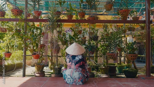 Asian person in conical hat working in the garden. Back view. Distant view. photo